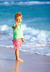 Wall Mural - cute boy on beach, showing victory gesture