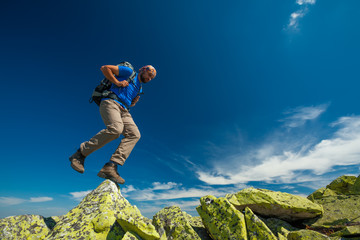 Wall Mural - Hiker jumps over stones in mountains