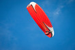 Red paraglider flying in blue sky.