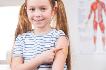 Vaccination. Cheerful little girl holding finger on the arm and