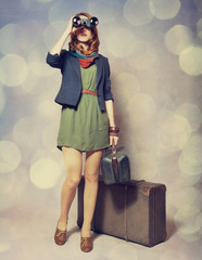 Redhead girl with binocular standing near the big suitcase