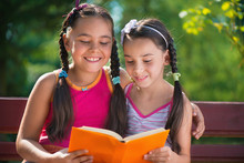 Sisters Reading Book In Summer Park