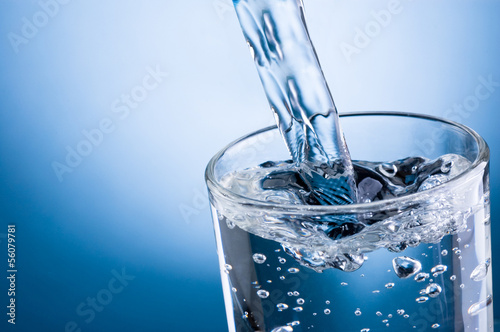 Plakat na zamówienie Pouring water into glass on blue background