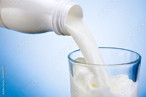 Fotografie, Obraz Pouring milk from white plastic bottle into glass on blue backgr