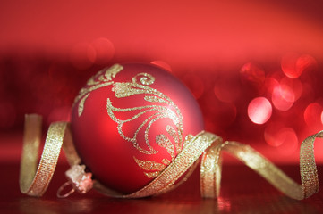 Wall Mural - red xmas ball with golden ribbon on red blurred background