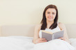 © WavebreakmediaMicro - Smiling girl looking at camera and reading a book lying on a bed