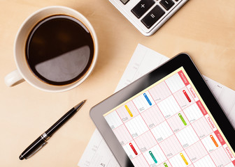 Tablet pc showing calendar on screen with a cup of coffee on a d