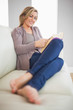 © WavebreakmediaMicro - Smiling woman lying on a sofa reading a book