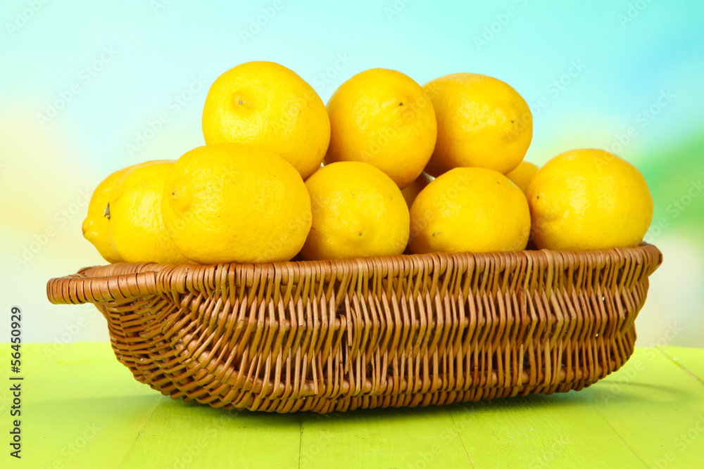 Ripe lemons in wicker basket on table on bright background