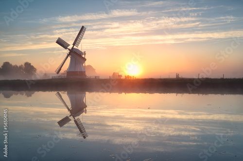Fotografija Dutch windmill reflected in river at sunrise