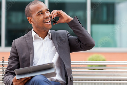Fotografie, Obraz Afro American manager sitting on the bench and phoning