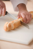 Fototapeta Kosmos - Cutting bread. Close-up top view of chef cutting fresh bread