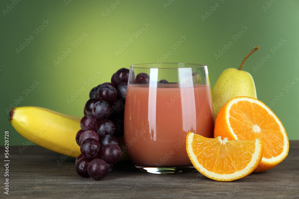 Glass of fresh juice on table on green background