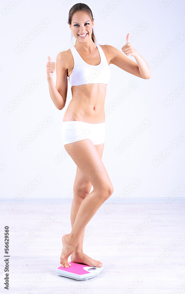 Slim young girl on scales on gray background
