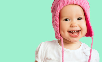 Wall Mural - Funny happy baby girl in a pink  winter knitted hat laughing