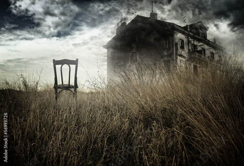 Fotografie, Obraz Abandoned chair out in a field facing a haunted house