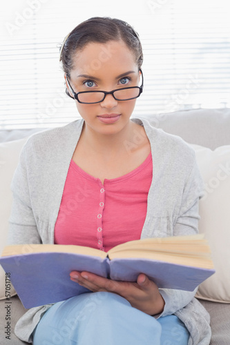 Fotografía Serious woman with reading glasses sitting on sofa and holding a