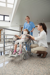 Wall Mural - Mother crouching next to her child in wheelchair with nurse push