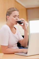 Poster - Portrait of a young woman using a laptop while drinking red wine