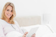 © WavebreakMediaMicro - Woman in bed with tablet pc in hand looking up and smiling