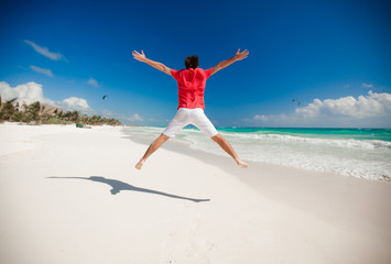 Wall Mural - Young man jumping and raising his arms up on the beach