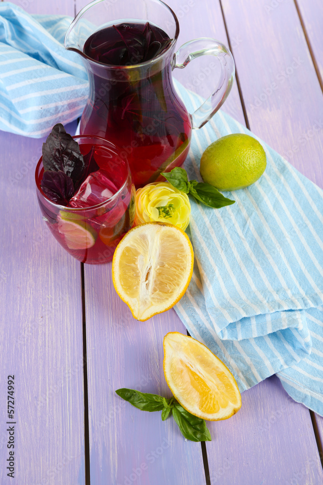 Red basil lemonade in jug and glass, on wooden background