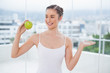 © lightwavemedia - Smiling sporty brunette holding green healthy apple