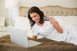 © lightwavemedia - Joyful pretty brown haired woman shopping online with her laptop
