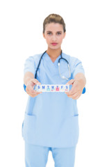 Wall Mural - Serious brown haired nurse in blue scrubs showing a medication b