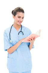 Wall Mural - Joyful brown haired nurse in blue scrubs holding a book