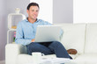 © WavebreakMediaMicro - Content casual man sitting on couch using laptop looking at came