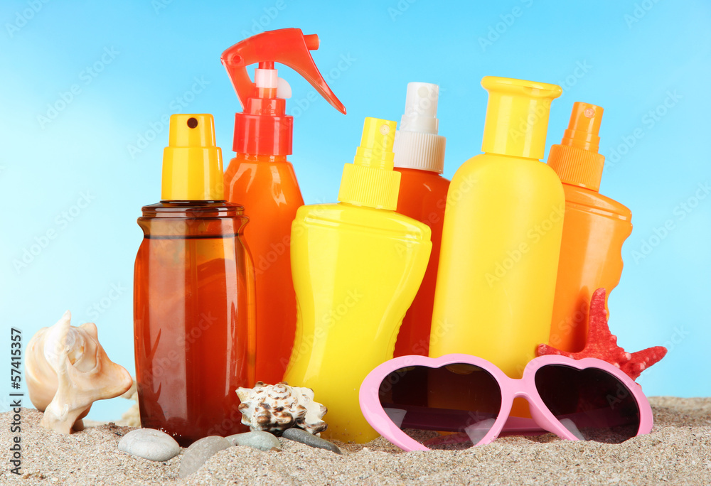 Bottles with suntan cream and sunglasses, on blue background