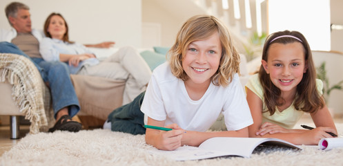Poster - Siblings doing their homework on the floor with parents behind t