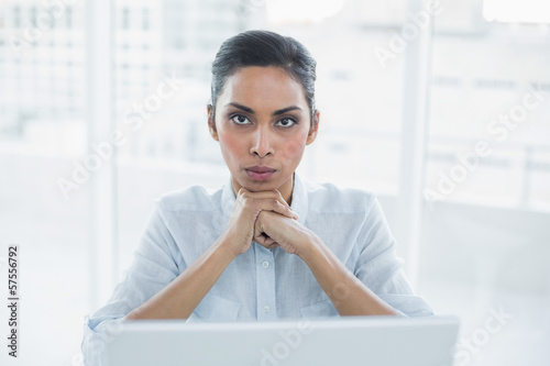 Fotografía Stern businesswoman sitting at her desk looking at camera