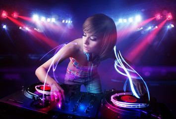 Disc jockey girl playing music with light beam effects on stage