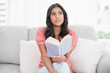 © lightwavemedia - Thoughtful cute brunette sitting on couch reading a book