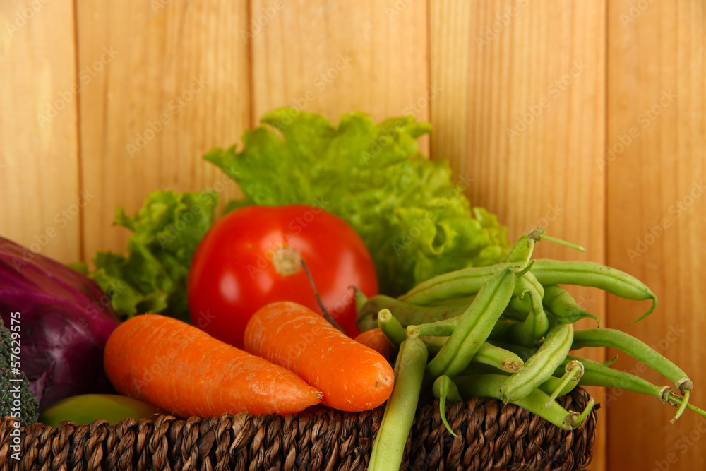 Different vegetables in basket on wooden background