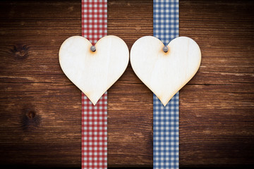 two wooden hearts on dark wood planks with red and blue ribbon