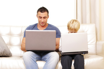 Father and son working on their computers on the sofa at home