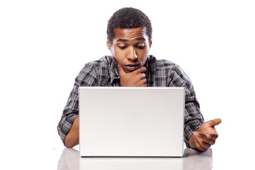 dark-skinned young man puzzled looking at his laptop