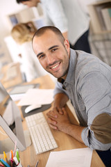 Wall Mural - Cheerful guy sitting in front of desktop computer