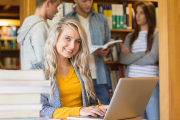 Poster - Female student using laptop while others in background at librar