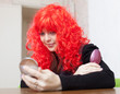 Woman in red wig stares into mirror