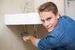 © lightwavemedia - Smiling plumber repairing washbasin drain