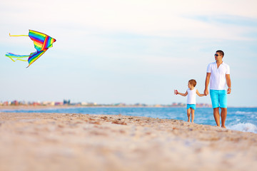 Wall Mural - happy father and son playing with kite on summer beach