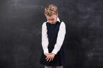 Sad little schoolgirl near blackboard