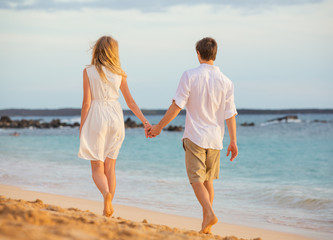 Romantic happy couple walking on beach at sunset. Smiling holdin