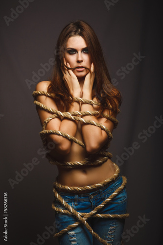Fotografía brunette woman bound with rope prisoner in jeans on a gray backg