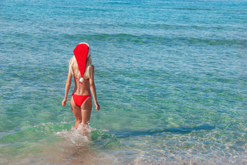 Wall Mural - Beautiful blonde woman in red christmas hat on sea beach. New ye