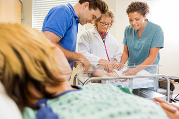 Fototapete - Doctor Examining Baby By Nurse And Man With Mother In Foreground